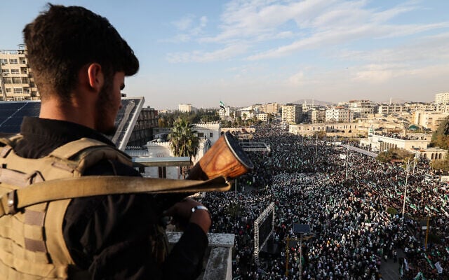 A member of the Syrian security forces stands guard from a position overlooking crowds during celebrations marking one year since a lightning Islamist-led offensive that eventually toppled the country's longtime ruler Bashar al-Assad, in central Hama on December 5, 2025. (OMAR HAJ KADOUR / AFP) A member of the Syrian security forces stands guard from a position overlooking crowds during celebrations marking one year since a lightning Islamist-led offensive that eventually toppled the country's longtime ruler Bashar al-Assad, in central Hama on December 5, 2025. (OMAR HAJ KADOUR / AFP)