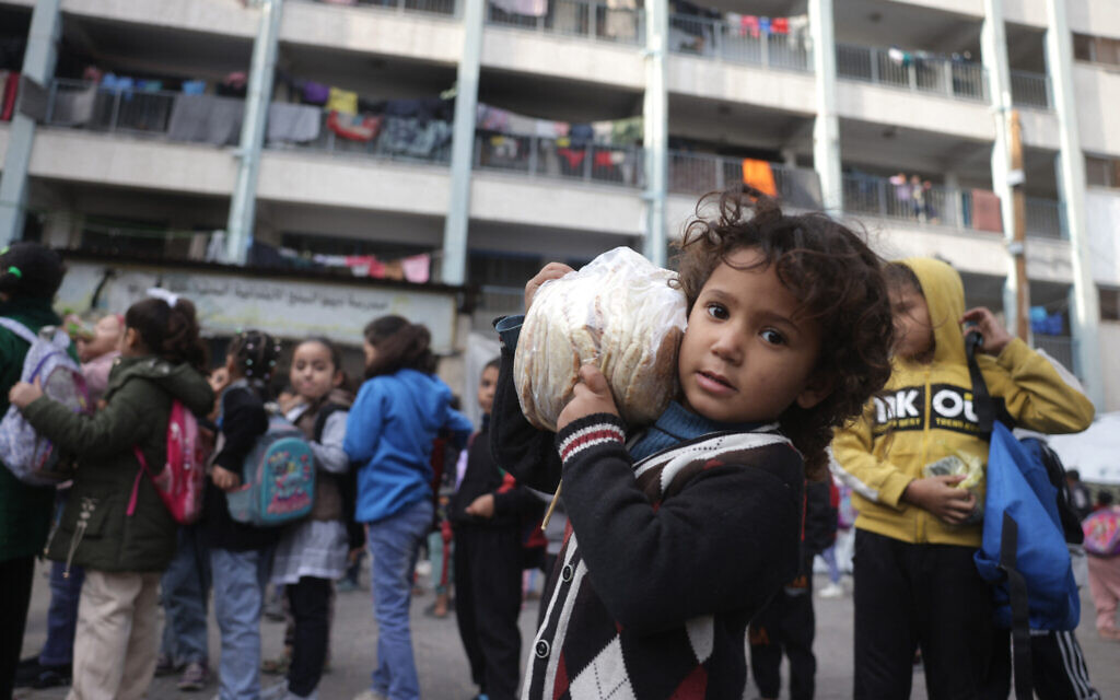 A Palestinian girl carries a bag of bread as others, many of whom are part of displaced families, gather in the yard of the UNRWA Deir al-Balah Joint School, west of Deir al-Balah, in the central Gaza Strip, December 6, 2025. (Bashar Taleb/AFP) A Palestinian girl carries a bag of bread as others, many of whom are part of displaced families, gather in the yard of the UNRWA Deir al-Balah Joint School, west of Deir al-Balah, in the central Gaza Strip, December 6, 2025. (Bashar Taleb/AFP)