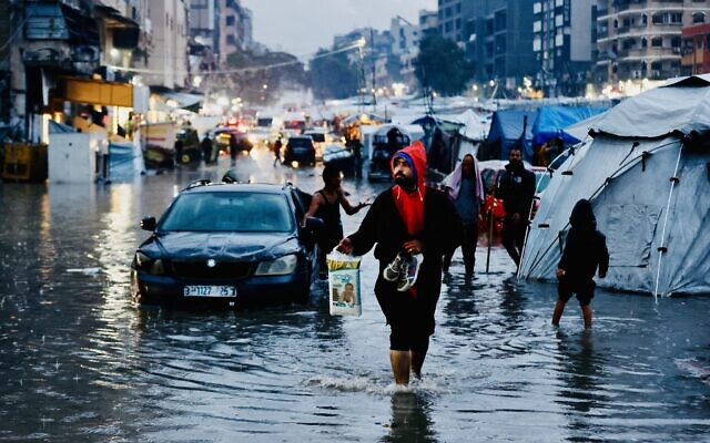 Palestinians walk through floodwaters following heavy rains in Gaza City on December 15, 2025 (Omar AL-QATTAA / AFP)