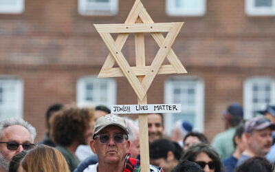 A mourner holds up a wooden Star of David with a sign reading 'Jewish Lives Matter' as people gather around floral tributes outside Bondi Pavilion in Sydney on December 16, 2025. (DAVID GRAY / AFP)