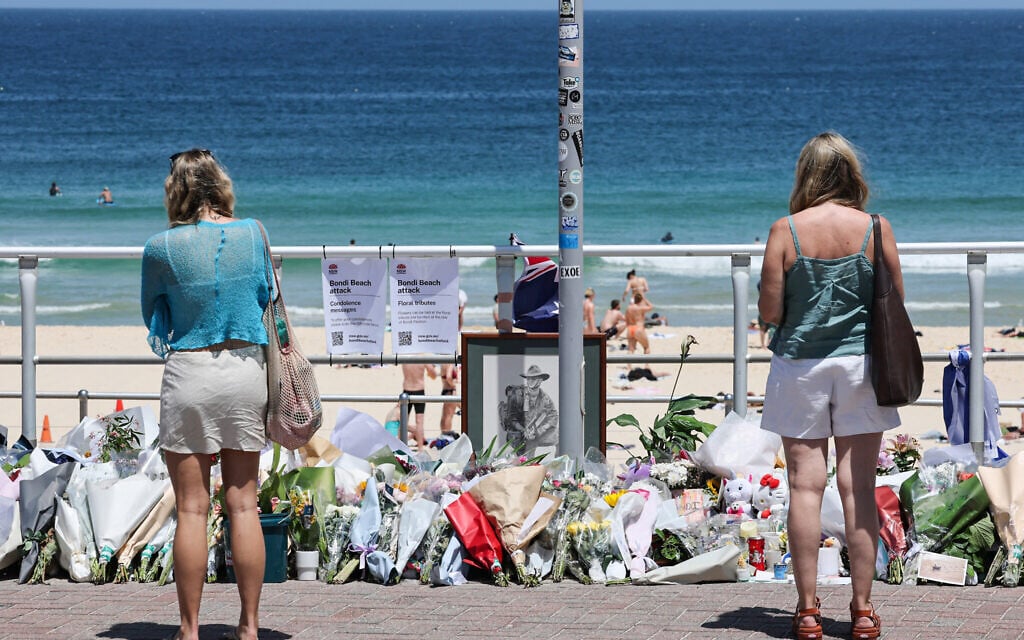 People stand in front floral tributes left at the promenade of Bondi Beach in Sydney on December 18, 2025, to honour victims of the terror shooting that targeted a Jewish event there on December 14, 2025. (DAVID GRAY / AFP)
