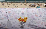 Beachgoers are seen behind a piece of cloth bearing messages left by mourners at the promenade of Bondi Beach in Sydney on December 18, 2025, to honor the victims of the terror attack that targeted a Jewish community event marking the first night of Hanukkah on December 14. (David Gray / AFP)