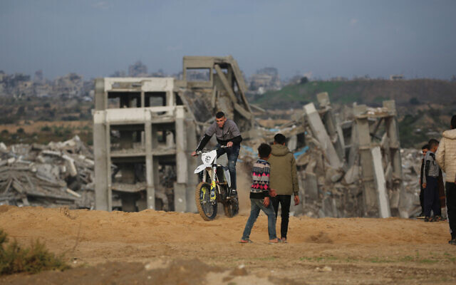 Displaced Palestinians watch as a motorcyclist rides on the sand dunes opposite destroyed buildings in Nuseirat camp in the central Gaza Strip on December 19, 2025. (Eyad Baba / AFP) Displaced Palestinians watch as a motorcyclist rides on the sand dunes opposite destroyed buildings in Nuseirat camp in the central Gaza Strip on December 19, 2025. (Eyad Baba / AFP)