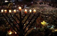 A menorah is pictured after the seventh candle is lit for the Jewish festival of Hanukkah as mourners stand next to floral tributes laid out in memory of the victims of a shooting attack at Bondi Beach, in Sydney, December 20, 2025. (David Gray / AFP)