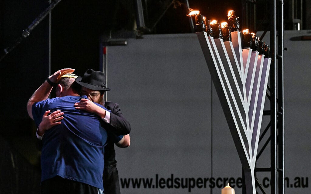 The father (left) of 10-year-old Matilda, who was killed in the December 14 Bondi Beach terror attack targeting the Jewish community, is greeted on stage as he lights the eighth candle of a menorah during the memorial held for the victims of the attack on December 21, 2025. (Saeed KHAN / AFP)