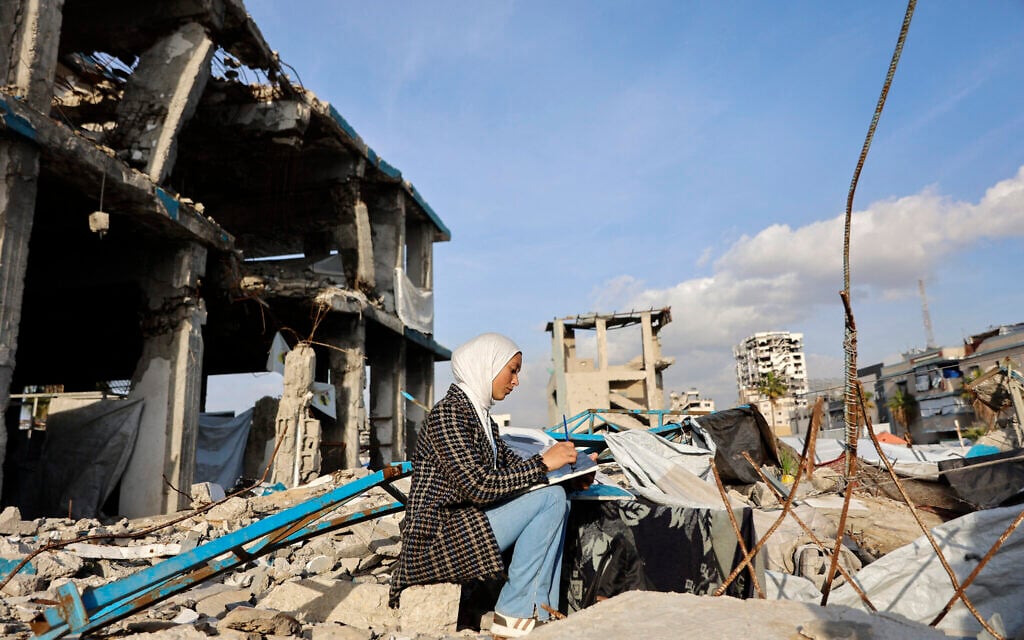 Fifteen-year-old displaced Palestinian Sarah Saada, who fled Beit Lahia in the northern Gaza Strip during Israeli strikes, paints amid the rubble of destroyed buildings in Gaza City, on December 30, 2025 (Omar AL-QATTAA / AFP)