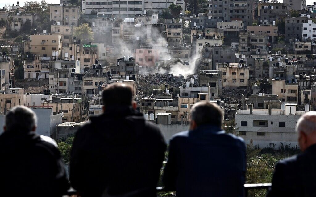 Residents of the Nur Shams Palestinian refugee camp watch their homes being demolished on New Year's eve by an Israeli military excavator in the Nur Shams camp, east of the northern West Bank city of Tulkarem, amid an ongoing offensives in the West Bank on December 31, 2025. (Photo by Zain JAAFAR / AFP)