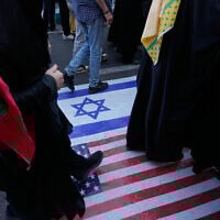 Demonstrators walk on a representation of the US and Israeli flags during an annual rally in front of the former US Embassy in Tehran, celebrating the anniversary of the 1979 takeover of the embassy, Iran, November 4, 2025. (AP Photo/Vahid Salemi)