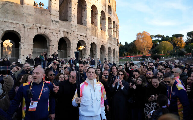 Italian singer Achille Lauro carries the 2026 Milan Cortina Winter Olympics torch in front of the Colosseum in Rome, along its journey through Italy, December 6, 2025. (AP Photo/Gregorio Borgia)