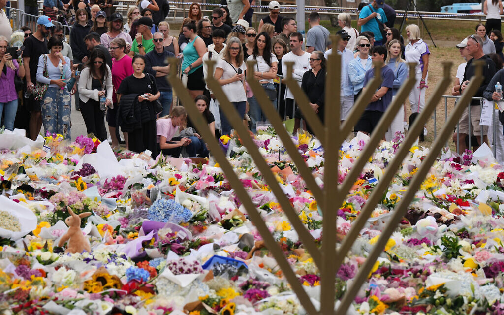 A Hanukkah menorah stands by a floral tribute as people gather to pay their respects near the Bondi Pavilion at Bondi Beach on December 16, 2025, following the deadly terror shooting targeting a Hanukkah event in Sydney, Australia. (AP/Mark Baker)
