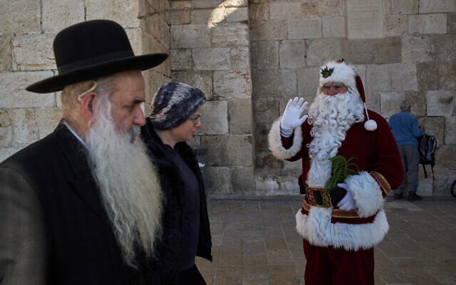 Illustrative: Issa Kassissieh, 47, who has dressed up as Santa Claus for 18 years, waves to the people during his annual tour of the Old City of Jerusalem, December 18, 2025. (AP/Leo Correa)