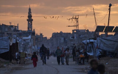 Palestinian youth walk along a tent camp for displaced people as the sun sets in Nuseirat, central Gaza Strip, December 26, 2025. (AP/Abdel Kareem Hana)