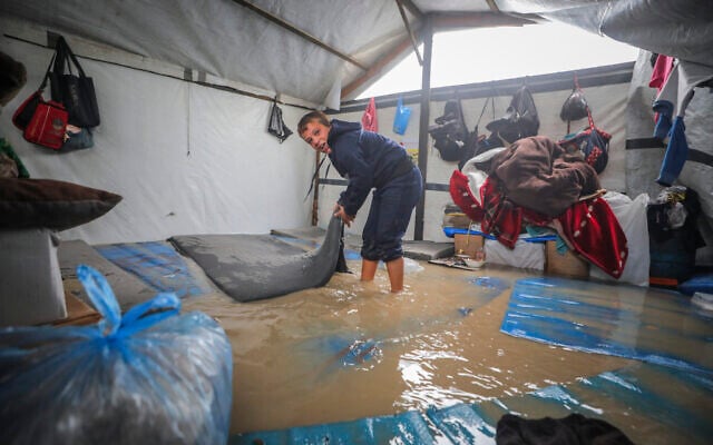A Palestinian boy wades through a flooded tent in the Nuseirat Refugee Camp in central Gaza, on December 12, 2025ץ (Ali Hassan/Flash90)