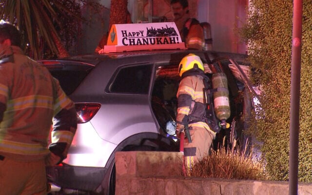Australian officials examine a car bearing a 'Happy Chanukah' sign whose interior was torched, reportedly using a firebomb, in Melbourne's St. Kilda East neighborhood, December 24, 2025. (Screenshot; used in accordance with Clause 27a of the Copyright Law)