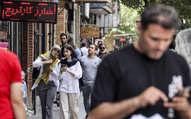 People walk along a street, some while browsing phones, in Tehran, Iran, on September 4, 2023. (ATTA KENARE / AFP)