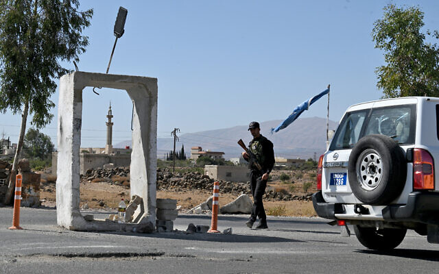 A United Nations Disengagement Observatory Force (UNDOF) vehicle drives past a member of Syria's security forces standing guard outside a former army base near the city of Quneitra in southern Syria, on the edge of the Golan Heights on September 21, 2025 (LOUAI BESHARA / AFP)