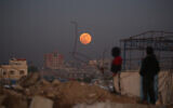 Illustrative: Displaced Palestinian children look at the first supermoon of the year, the 'Wolf Moon,' as it rises over the Bureij refugee camp in the central Gaza Strip on January 3, 2026. (Eyad Baba/AFP)