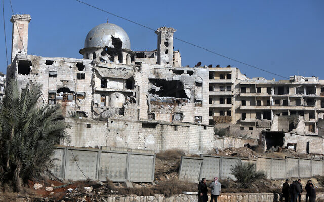 Residents of Sheikh Maqsoud neighborhood stand against the backdrop of damaged buildings, in Aleppo on January 10, 2026. (Bakr ALkasem / AFP)