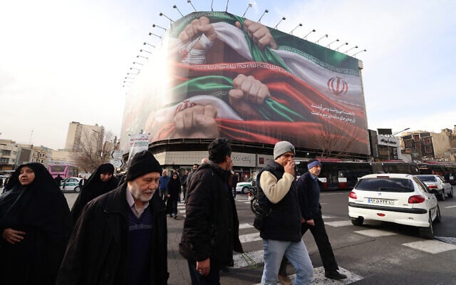 People walk past a large patriotic banner depicting the Iranian flag in Enghelab Square in Tehran on January 14, 2026. (ATTA KENARE / AFP) People walk past a large patriotic banner depicting the Iranian flag in Enghelab Square in Tehran on January 14, 2026. (ATTA KENARE / AFP)