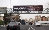 Commuters drive under a banner that reads 'this is not a protest' next to a picture of a burnt-out bus, in Tehran, Iran, on January 15, 2026. (ATTA KENARE / AFP)