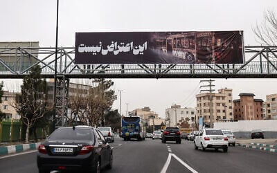 Commuters drive under a banner that reads 'this is not a protest' next to a picture of a burnt-out bus, in Tehran, Iran, on January 15, 2026. (ATTA KENARE / AFP)