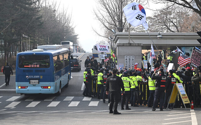 A blue bus believed to be transporting South Korea's impeached former president Yoon Suk Yeol arrives at the Seoul Central District Court in Seoul on January 16, 2026, as his supporters (R) gather in front of the court. (Jung Yeon-je / AFP)