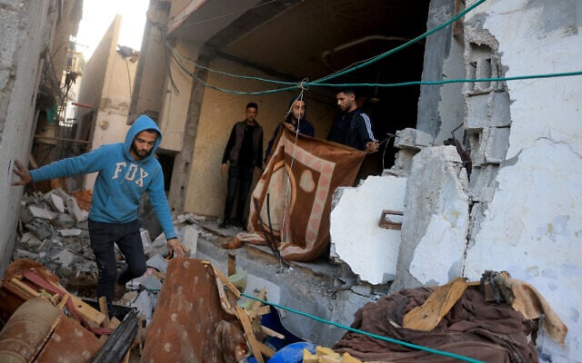 Palestinian men maneuver past debris and broken furniture, after an Israeli strike on the family home of Hamas military commander Muhammad al-Hawli,, west of Deir al-Balah, in the central Gaza Strip on January 16, 2026.  (Bashar Taleb/AFP)