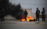 Kurdish fighters stand near burning tires at the entrance to the city of Tabqa in the northern Syrian Raqa province, on January 17, 2026. (Delil SOULEIMAN / AFP)