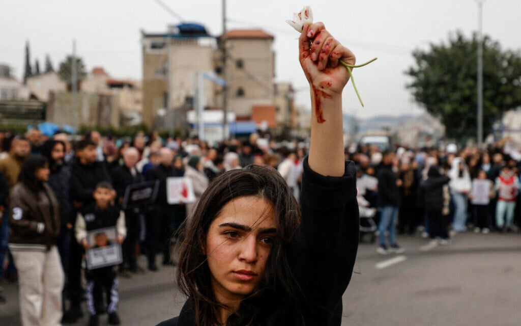 A woman raises flowers, with red marks visible on her hand, as Arab protesters gather in Sakhnin in northern Israel, on January 22, 2026, to protest what they say is police inaction on curbing soaring violent crime in the community. (Jalaa MAREY / AFP)
