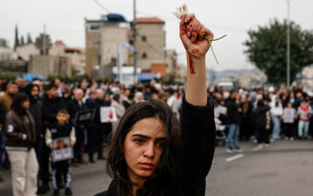 A woman raises flowers, with red marks visible on her hand, as Arab protesters gather in Sakhnin in northern Israel, on January 22, 2026, to protest what they say is police inaction on curbing soaring violent crime in the community. (Jalaa MAREY / AFP)