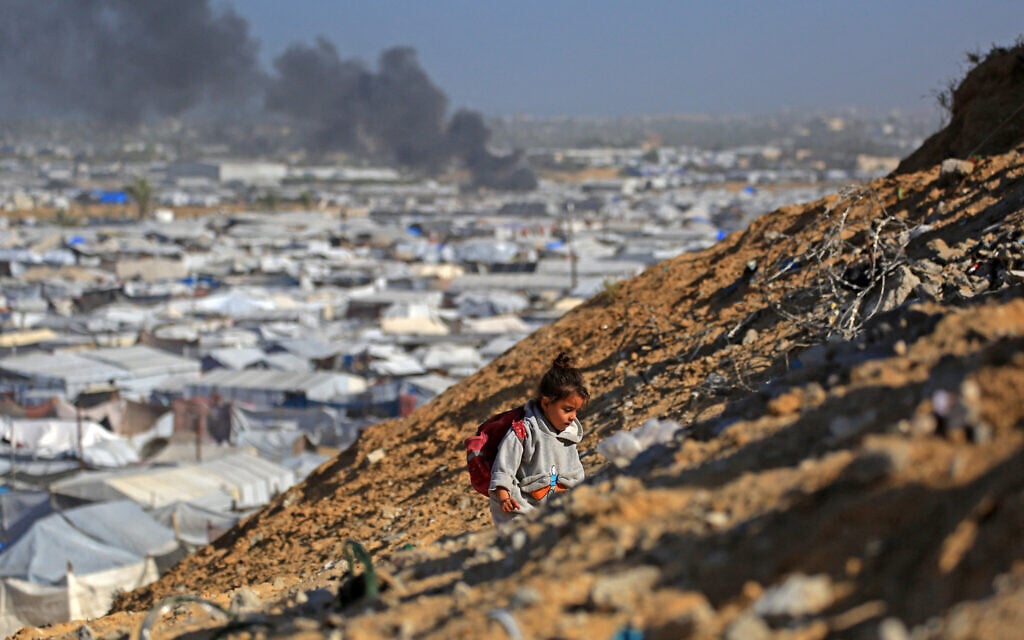 A girl climbs a hilltop against the backdrop of tents housing displaced people, and smoke rising after an Israeli airstrike, in the west of Khan Younis, southern Gaza Strip on January 31, 2026. (Bashar Taleb / AFP)