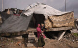 A woman holds a child as they stand in front of their tent in a makeshift camp for displaced Palestinians set up in an area in Gaza City, December 29, 2025. (AP/Jehad Alshrafi)