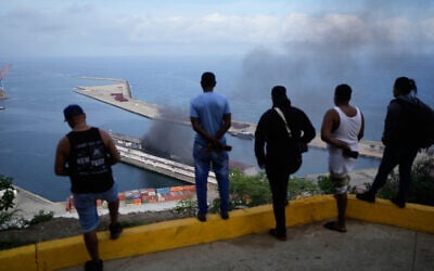 People watch smoke rising from a dock after a series of US strikes at La Guaira port, Venezuela, January 3, 2026. (AP/Matias Delacroix) People watch smoke rising from a dock after a series of US strikes at La Guaira port, Venezuela, January 3, 2026. (AP/Matias Delacroix)