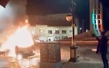 This frame grab from a video released January 9, 2026, by Iranian state television shows a man holding a device to document burning vehicles during a night of mass protests in Zanjan, Iran. (Iranian state TV via AP)