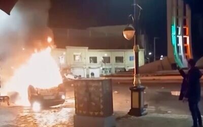 This frame grab from a video released January 9, 2026, by Iranian state television shows a man holding a device to document burning vehicles during a night of mass protests in Zanjan, Iran. (Iranian state TV via AP)