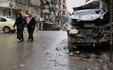 Women walk by a damaged car in the predominantly Kurdish Sheikh Maqsoud neighborhood after days of fighting between government forces and Kurdish fighters in the northern city of Aleppo, Syria, January 13, 2026. (AP Photo/Ghaith Alsayed)