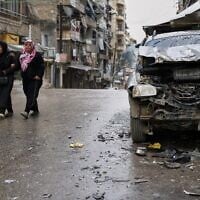 Women walk by a damaged car in the predominantly Kurdish Sheikh Maqsoud neighborhood after days of fighting between government forces and Kurdish fighters in the northern city of Aleppo, Syria, January 13, 2026. (AP Photo/Ghaith Alsayed)