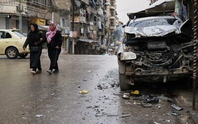 Women walk by a damaged car in the predominantly Kurdish Sheikh Maqsoud neighborhood after days of fighting between government forces and Kurdish fighters in the northern city of Aleppo, Syria, January 13, 2026. (AP Photo/Ghaith Alsayed)