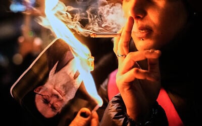 A protester smokes a cigarette after lighting it off a burning poster of Iran's Supreme Leader Ayatollah Ali Khamenei during a demonstration in Berlin, Germany, in support of the nationwide mass protests in Iran against the government, January 14, 2026. (AP Photo/Ebrahim Noroozi)