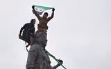 Syrian government soldiers wave a Syrian flag after climbing atop a statue of a female Kurdish fighter, following the takeover of the town from US-backed Syrian Democratic Forces (SDF) during an ongoing push against Kurdish-led forces, in Tabqa, eastern Syria, January 18, 2026. (AP Photo/ Omar Albam)