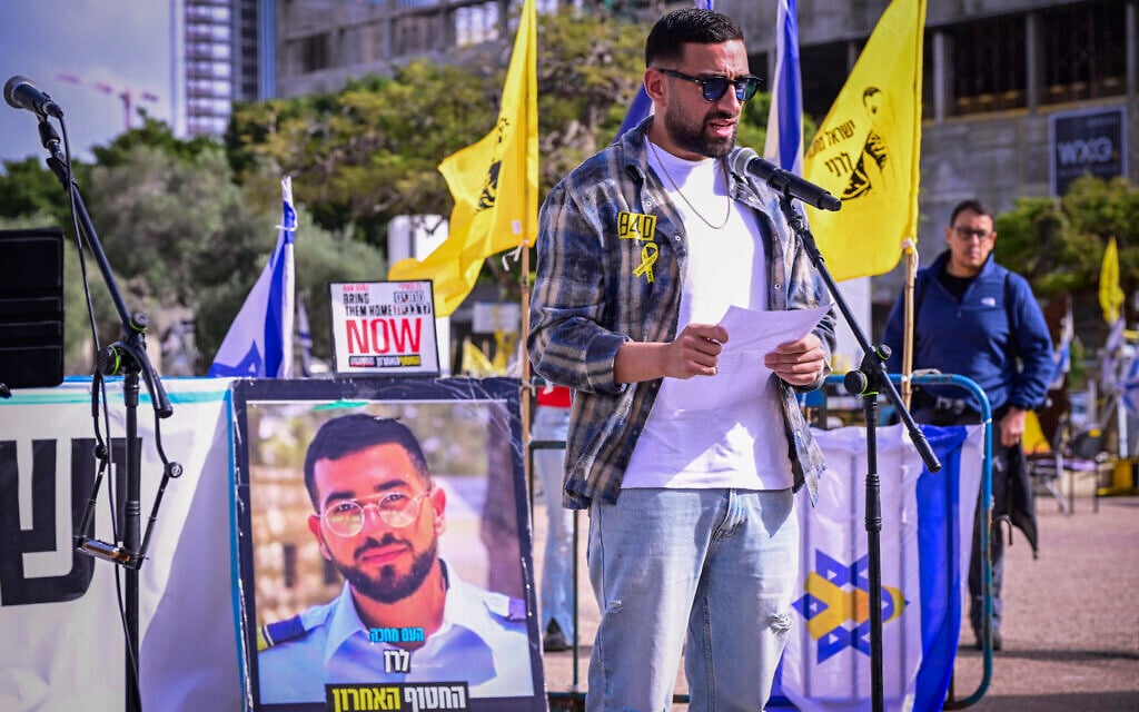 Former hostage Segev Kalfon speaks at a Friday afternoon gathering in honor of the last hostage in Gaza, Police Master Sgt. Ran Gvili, whose portrait is on display, at Tel Aviv's Hostages Square on January 23, 2026. (Avshalom Sassoni/Flash90)