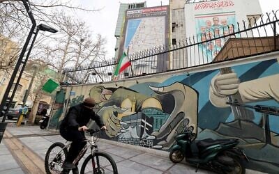 A man cycles past a mural and a giant billboard displaying a map of potential targets in the Tel Aviv area along with a warning message reading, 'You start, we finish!' in Palestine Square, in Tehran, Iran, on February 9, 2026. (ATTA KENARE / AFP)