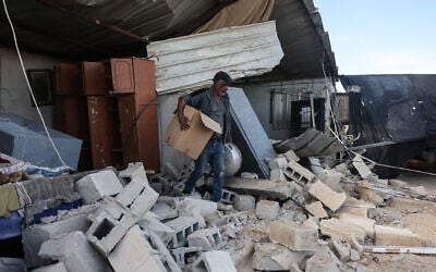 A Palestinian man carries a cardboard box as he stands on the rubble of a house that was reportedly demolished by Israeli settlers the previous day in Al-Duyuk Al-Tahta, a village on the outskirts of Jericho, in the West Bank, on February 11, 2026. (AHMAD GHARABLI / AFP)