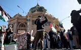 A protester speaks through a megaphone as he stands with others holding flags and banners outside Flinders Street station during the visit of Israel's President Isaac Herzog in Melbourne on February 12, 2026. (MARTIN KEEP / AFP)
