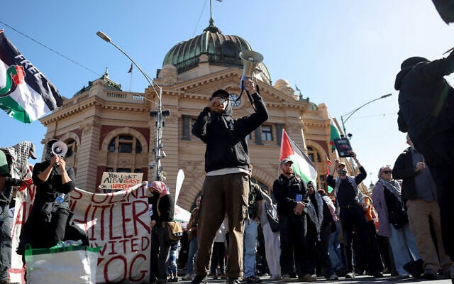 A protester speaks through a megaphone as he stands with others holding flags and banners outside Flinders Street station during the visit of Israel's President Isaac Herzog in Melbourne on February 12, 2026. (MARTIN KEEP / AFP) A protester speaks through a megaphone as he stands with others holding flags and banners outside Flinders Street station during the visit of Israel's President Isaac Herzog in Melbourne on February 12, 2026. (MARTIN KEEP / AFP)