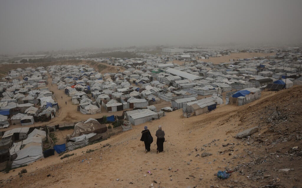 Women walk down a hill overlooking a camp for displaced Palestinians on a foggy day in Khan Younis, in the southern Gaza Strip, on February 14, 2026 (Bashar Taleb / AFP)