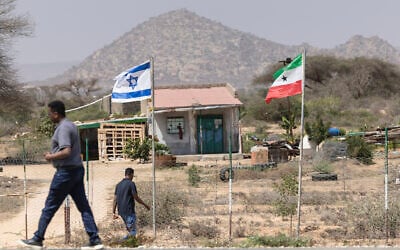 People walk by the flags of Israel and Somaliland flying alongside each other at the entrance to a fruit farm between the capital city of Hargeisa and Port city of Berbera along the highway connecting the two as Muslims commemorate the holy month of Ramadan in Somaliland on February 19, 2026. (Tony KARUMBA / AFP)