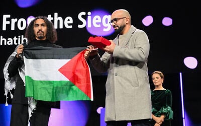 Syrian-Palestinian director Abdullah Al-Khatib (L) and Algerian producer Taqiyeddine Issaad hold a Palestinian flag as they accept the GWFF Best Feature Film Debut Award for "Chronicles From the Siege" during the Award Ceremony of the 76th Berlinale, Europe's first major film festival of the year, in Berlin on February 21, 2026. (RALF HIRSCHBERGER / AFP)