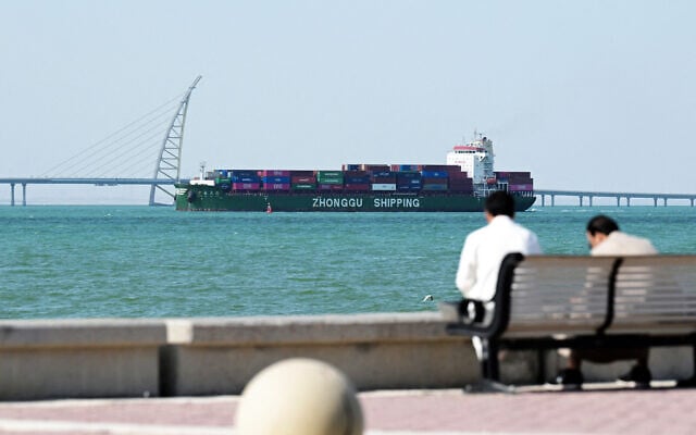 People sit on a bench on the Sheikh Jaber al-Ahmad al-Sabah Causeway as a Zhonggu Shipping container ship sails past on its way towards the port of Shuwaikh in Kuwait City on February 28, 2026. (Photo by YASSER AL-ZAYYAT / AFP) People sit on a bench on the Sheikh Jaber al-Ahmad al-Sabah Causeway as a Zhonggu Shipping container ship sails past on its way towards the port of Shuwaikh in Kuwait City on February 28, 2026. (Photo by YASSER AL-ZAYYAT / AFP)