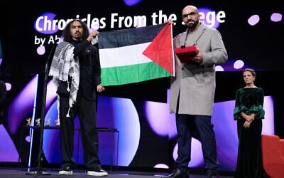 Director Abdallah Al-Khatib, left, and Taqiyeddine Issaad hold a Palestinian flag after receiving the GWFF best first feature award for 'Chronicles from the Siege,' during the awards ceremony for the International Film Festival, Berlinale, in Berlin, Germany, February 21, 2026. (Ebrahim Noroozi/ AP).